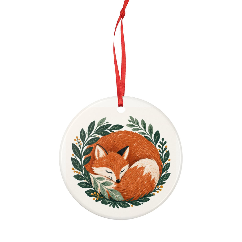 Round ceramic hanging ornament showing sleeping russet fox curled among green woodland leaves.