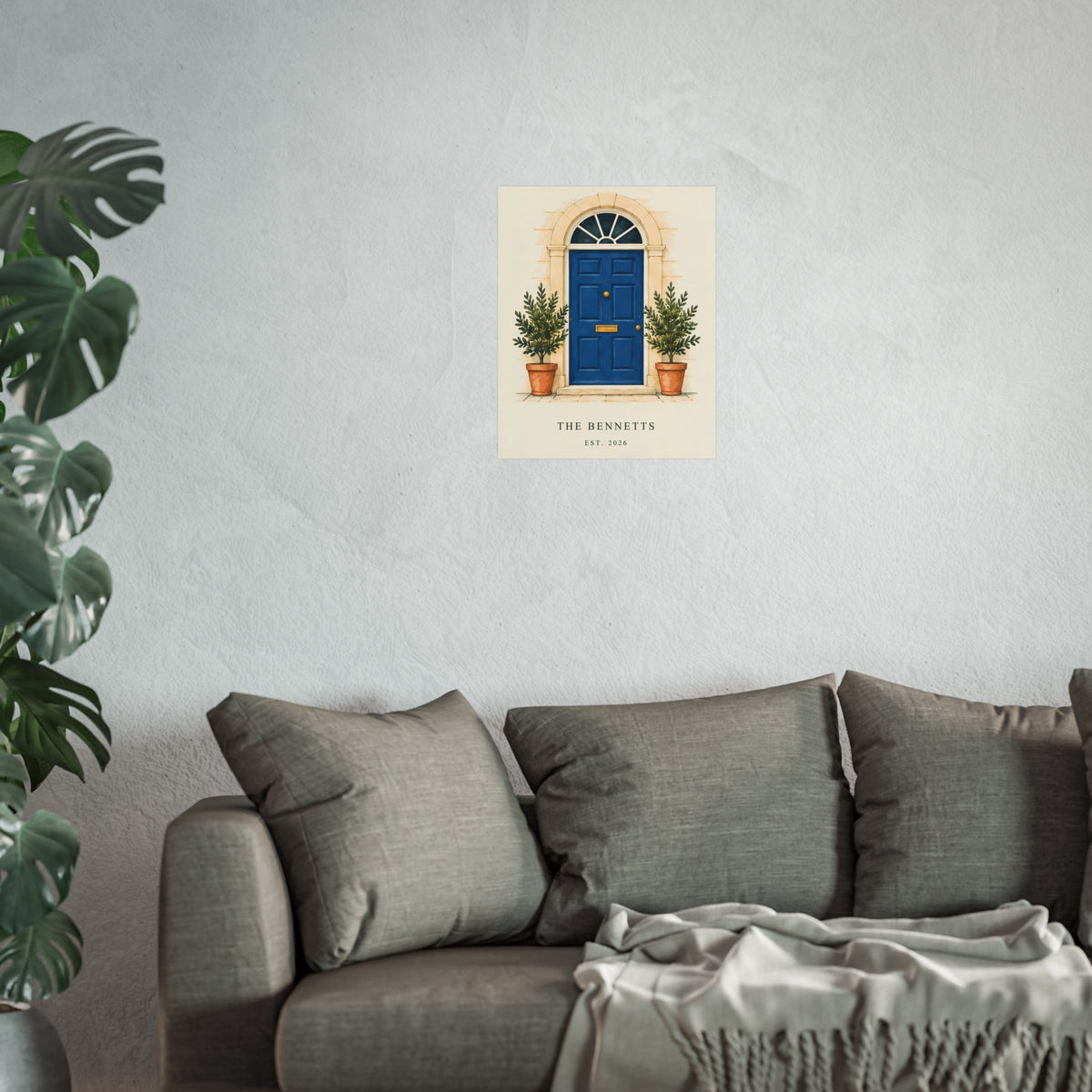 Our Little Door personalised blue-door art print with example household wording, shown on a pale wall above a grey sofa for scale