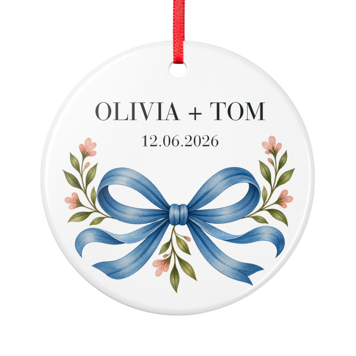 Round ceramic hanging ornament showing blue illustrated bow and pink flowers beneath sample names Olivia + Tom and a sample date.