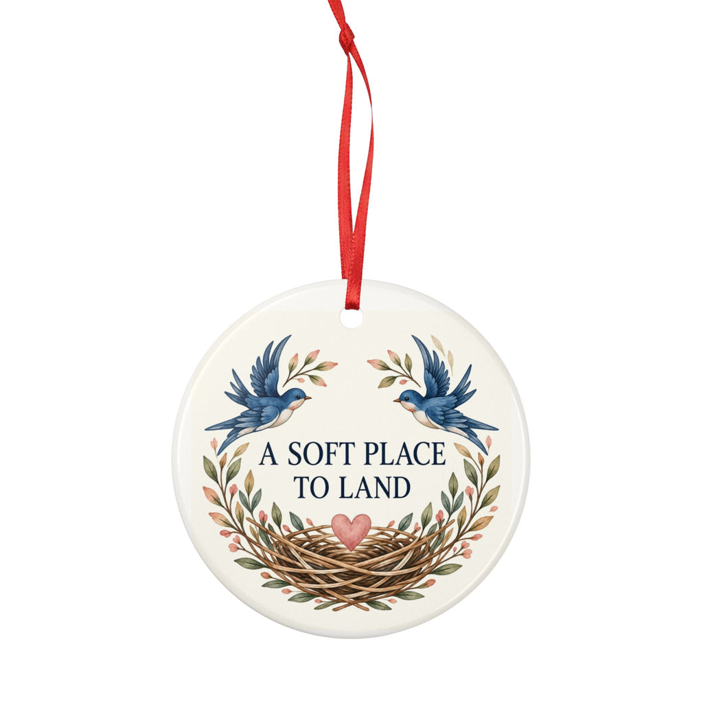 Round ceramic hanging ornament showing two blue birds, botanical sprigs, a nest and A Soft Place to Land lettering.
