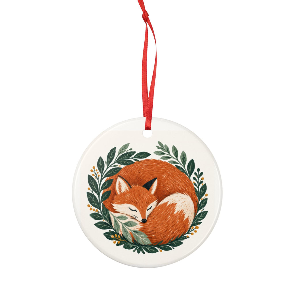 Round ceramic hanging ornament showing sleeping russet fox curled among green woodland leaves.