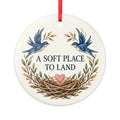 Round ceramic hanging ornament showing two blue birds, botanical sprigs, a nest and A Soft Place to Land lettering.