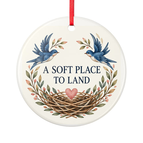 Round ceramic hanging ornament showing two blue birds, botanical sprigs, a nest and A Soft Place to Land lettering.