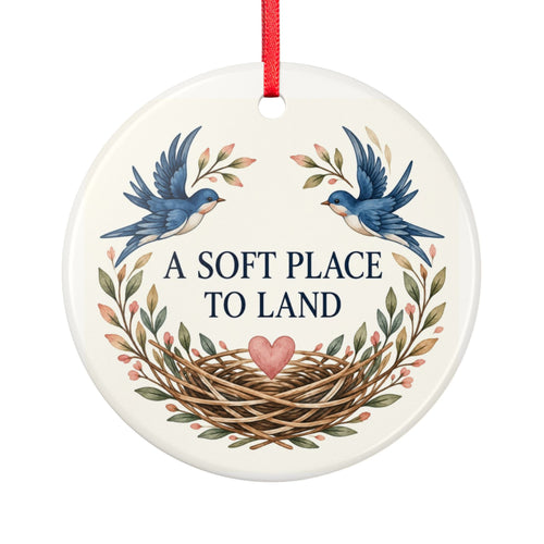 Round ceramic hanging ornament showing two blue birds, botanical sprigs, a nest and A Soft Place to Land lettering.