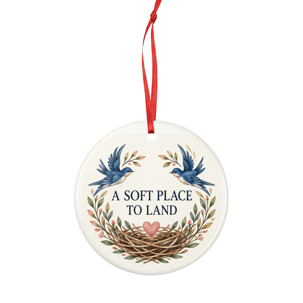 Round ceramic hanging ornament showing two blue birds, botanical sprigs, a nest and A Soft Place to Land lettering.
