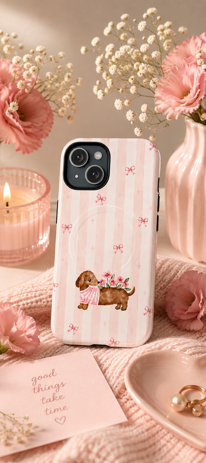 Dachshund and Flowers phone case with pink stripes and bows, styled beside flowers, a candle and pink knit fabric.