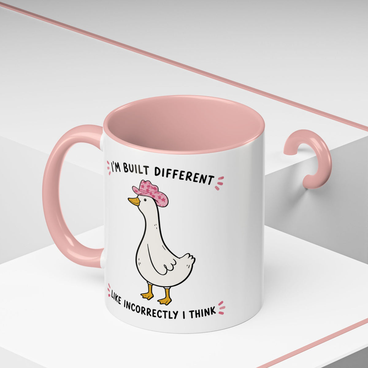 Pink Built Different duck mug on a geometric display