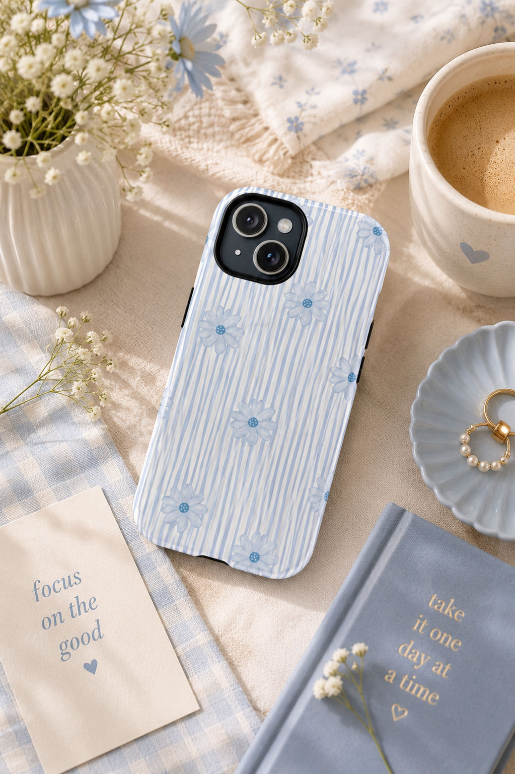 Blue Ditsy Floral phone case with fine blue stripes and daisies, styled beside coffee, flowers and a blue notebook.