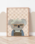 Bring Me Sunshine print showing a koala in sunglasses, a bow headband and dungarees against peach checks, displayed in a frame.