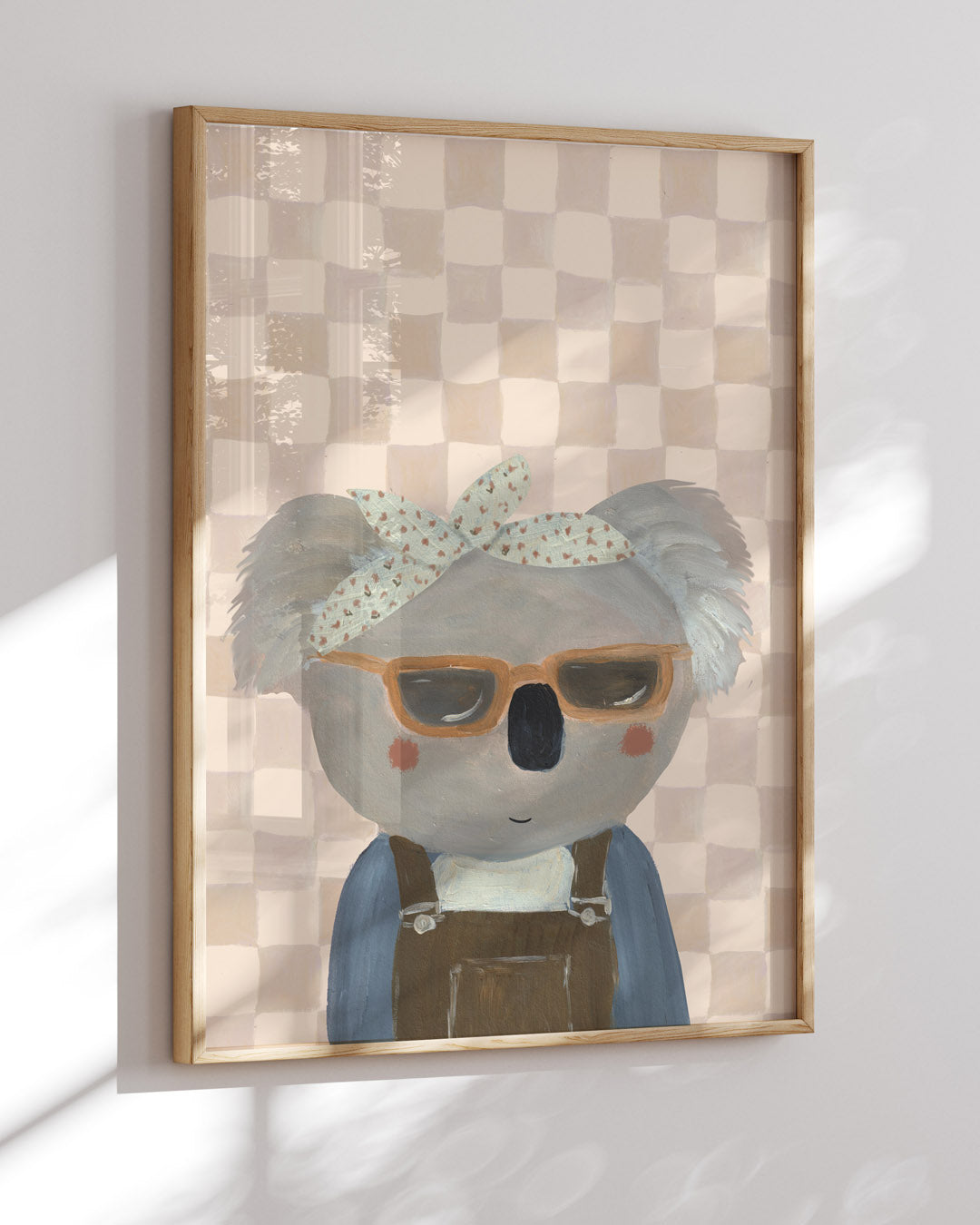 Close view of the sunglasses-wearing koala print in a wooden frame, with window light across the checked background.