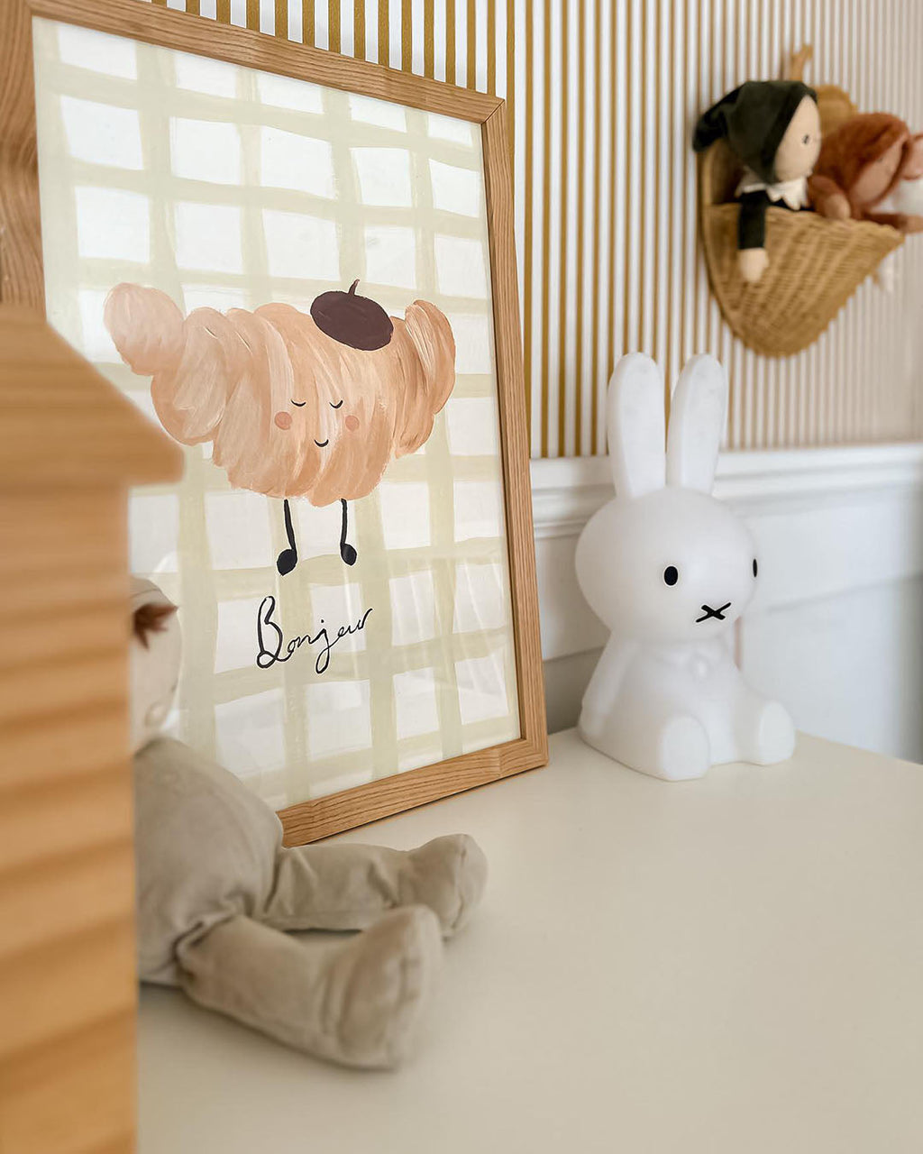 Close view of the Croissant print in a wooden frame beside a white rabbit ornament on a nursery shelf.